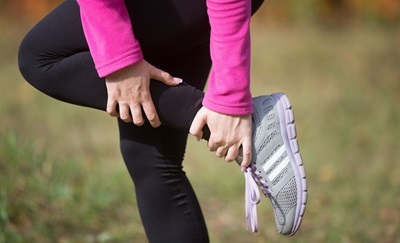 En kvinde i løbetøj holder sig til sit ben, fordi hun har fået en idrætsskade