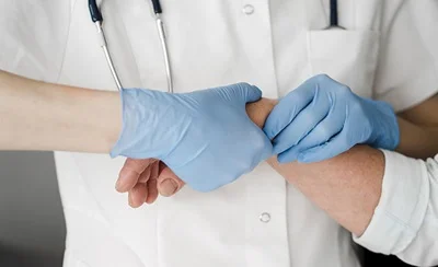 Udsnit af ortopædkirurgisk specialist i kittel, iført engangshandsker, der laver forundersøgelse af håndled på en patient.