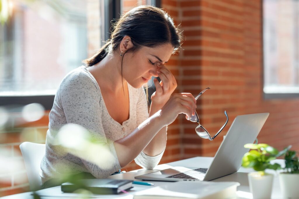 Træt kvinde med migræne, foran en bærbar computer