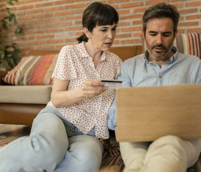 Middel aldrende par, som sidder hjemme på gulvet foran sofa og bruger bruger bærbar computer til at undersøge behandlingstilbud