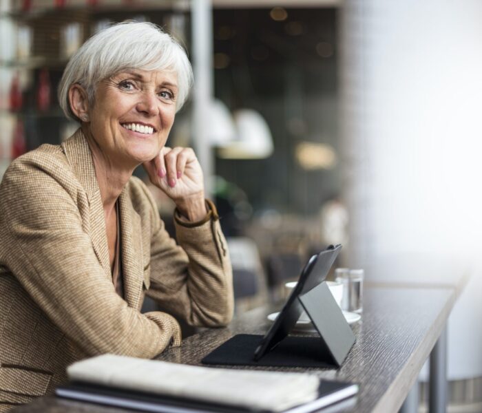 Portræt af smilende ældre forretningskvinde med tablet på en café